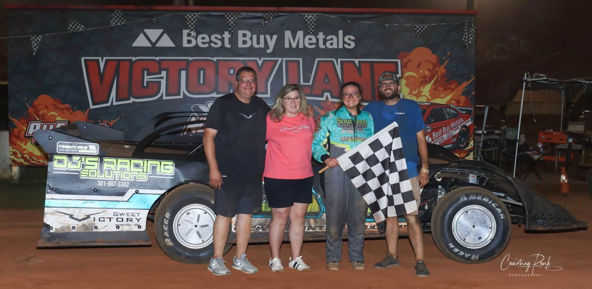 Olivia Gentry Williams in her racing suit holding the checkered flag in Victory Lane beside her dirt late model